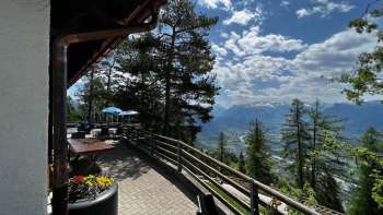 "Terrazza soleggiata con vista panoramica sulla valle del Reno nelle giornate limpide e accoglienti posti a sedere in stile alpino nella Berggasthaus Matu".