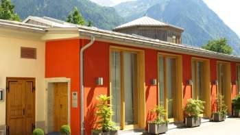 Vista esterna del Centro culturale Gasometro con la facciata colorata e il panorama alpino sullo sfondo.