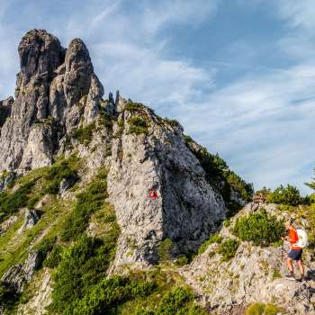Escursionisti su un sentiero roccioso di montagna davanti a una cresta impervia con un cartello rosso e bianco