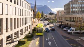 Un autobus LIEmobil attraversa Vaduz sullo sfondo delle Alpi e dell'architettura moderna