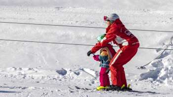 Una maestra di sci sale sulla seggiovia a piattello insieme a un bambino