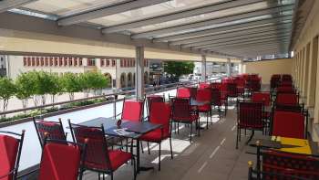 Terrazza soleggiata con sedie rosse e tavoli apparecchiati in bianco