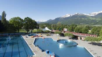 Vista generale della piscina all'aperto di Mühleholz con diverse vasche e un meraviglioso panorama alpino sullo sfondo.