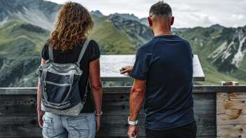 Una coppia osserva il cartello informativo sulla terrazza del rifugio Sareis.