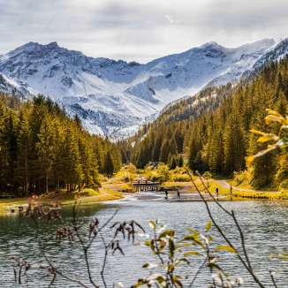 Atmosfera autunnale a Steg, nel Liechtenstein, con boschi colorati, un lago limpido e le Alpi innevate sullo sfondo