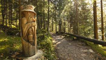 Figura in legno con lanterna al «sentiero delle leggende Walser» nella luce mistica della foresta