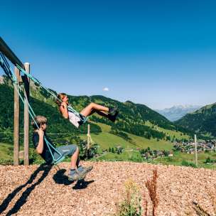 Due bambini che si dondolano in un parco giochi di montagna con vista sul panorama estivo di Malbun in Liechtenstein
