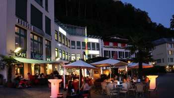 Atmosfera serale davanti alla Brasserie Burg di Vaduz con terrazza illuminata e ospiti sotto gli ombrelloni.