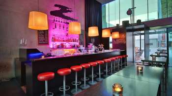 Bar moderno con banconi lunghi, sgabelli rossi e illuminazione elegante in rosa e arancione