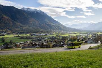 Autobus LIEmobil verde che percorre una strada tortuosa sopra il Liechtenstein con vista sulla valle del Reno e sulle Alpi circostanti