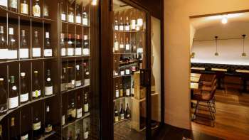 Moderna vetrina per vini con bottiglie pregiate nell'elegante WY Weinbar, vista sulla sala di degustazione adiacente.
