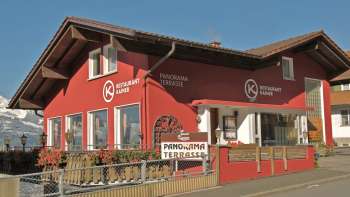 Edificio rosso del ristorante Kainer con balcone in legno e invitante area esterna Edificio rosso del ristorante Kainer con balcone in legno e invitante area esterna