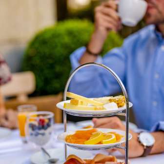 Colazione con salsiccia, formaggio e frutta fresca su un'etagere di Vaduz mentre un ospite beve un caffè