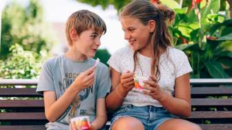 Due bambini siedono su una panchina del parco in Liechtenstein e mangiano un gelato - volti sorridenti, fiori e un'atmosfera estiva in campagna