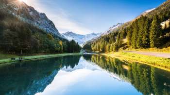 Lago Gänglesee a Steg con riflesso di montagna, circondato da boschi, raggi di sole sul pendio.