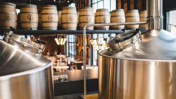 Vista di un moderno birrificio con serbatoi in acciaio inox scintillanti e botti di legno impilate sullo sfondo.