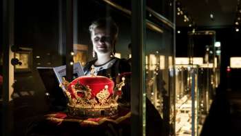 Giovane donna osserva una magnifica corona dietro un vetro nel museo nazionale del Liechtenstein.