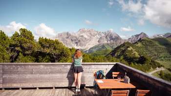 Una donna si gode la vista delle Alpi del Liechtenstein e della Valle del Reno dalla terrazza panoramica di Sareis in una giornata di bel tempo
