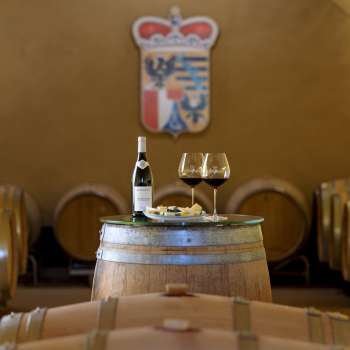 Suggestiva degustazione di vini nella cantina della Cantina Principesca con due bicchieri e una bottiglia di vino rosso su una botte di legno.