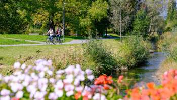 I ciclisti si godono il tempo soleggiato lungo le rive fiorite del Parco Naturale di Haberfeld.