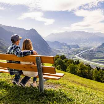 Coppia seduta su una panchina a Triesenberg e affacciata sulla valle del Reno in Liechtenstein con un impressionante panorama alpino