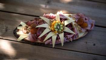 Una tavola di legno artisticamente disposta con vari tipi di salsiccia, formaggio e decorazioni di fiori commestibili, servita su un tavolo di legno. Una tavola di legno artisticamente disposta con vari tipi di salsiccia, formaggio e decorazioni di fiori commestibili, servita su un tavolo di legno.