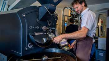 Uomo che tosta i chicchi di caffè su una moderna macchina per la tostatura in un impianto di tostatura del caffè
