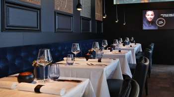 Eleganti interni dell'Esquire Bar & Bistro di Vaduz con tavoli apparecchiati con stile, panche imbottite blu scuro e illuminazione d'atmosfera.