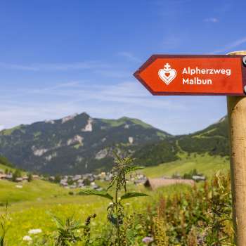 Cartello sentiero del cuore alpino con il villaggio di montagna di Malbun sullo sfondo