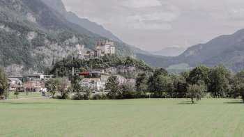 Maestosa vista della rocca di Gutenberg a Balzers, circondata da campi verdi e dalle imponenti Alpi.