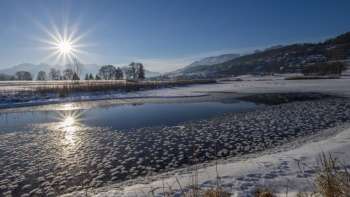 Alba sul lago Egelsee a Mauren in inverno, con ghiaccio scintillante, neve e uno sfondo di montagne soleggiate.