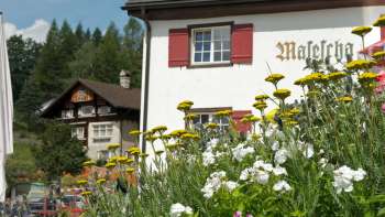 Tradizionale locanda di montagna con persiane rosse e fiori in primo piano Tradizionale locanda di montagna con persiane rosse e fiori in primo piano