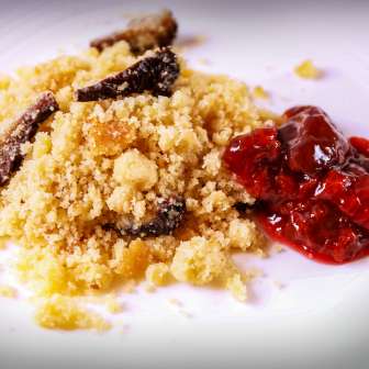 Piatto tradizionale Riebel del Liechtenstein con semolino di mais croccante e prugne dolci arrostite servito su un piatto bianco.