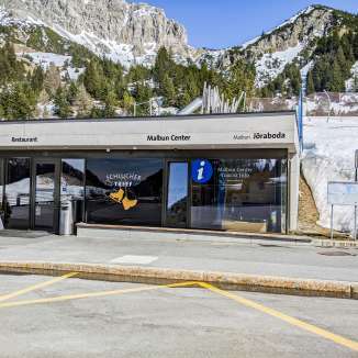 Ingresso del Centro di Malbun con informazioni turistiche e ristorante davanti a un paesaggio montano innevato a Malbun, Liechtenstein