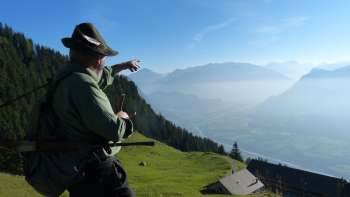Un uomo in abito tradizionale indica un prato di montagna nella valle del Reno. Un uomo in abito tradizionale indica un prato di montagna nella valle del Reno.