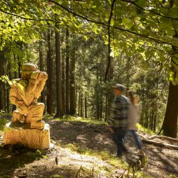 Gli escursionisti passano davanti a una figura scolpita con un binocolo sul «sentiero delle leggende Walser»