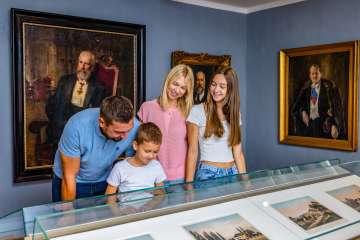 Una famiglia osserva i reperti esposti nel Museo nazionale del Liechtenstein a Vaduz, circondata da dipinti e ritratti storici.
