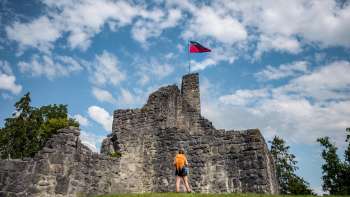 Un escursionista si trova di fronte alle imponenti rovine del castello di Schellenberg sotto un cielo azzurro