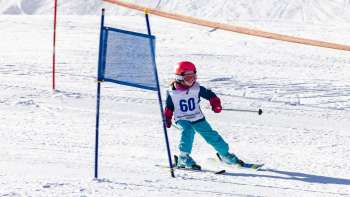 Un bambino con il numero di partenza attraversa con grande concentrazione i cancelli della gara di sci per bambini nell'Area giochi Malbi Park