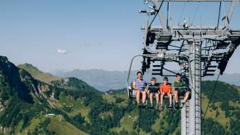 Una famiglia sale sulla seggiovia Sareis in un paesaggio montano verdeggiante Una famiglia sale sulla seggiovia Sareis in un paesaggio montano verdeggiante