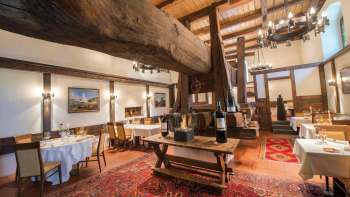 Sala da pranzo rustica con travi storiche in legno, camino e tavoli coperti nel ristorante Torkel.