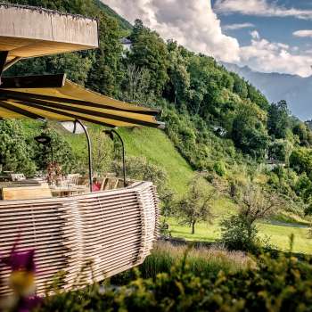 Terrazza soleggiata con fiori in fiore e tavoli elegantemente apparecchiati con vista sulla valle