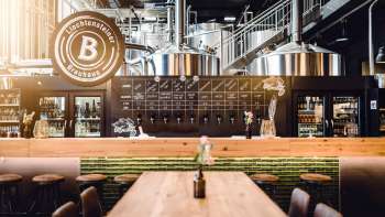 Accogliente taproom della Liechtensteiner Brauhaus con tavoli in legno, impianto di spillatura e vista sui bollitori di birra
