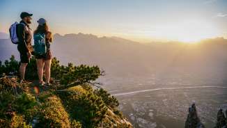 Tina Weirather e Marco Büchel si trovano sulla cima di una montagna e guardano la valle del Reno nel Liechtenstein al tramonto.